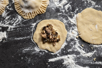 Preparation of gluten-free dumplings stuffed with mushrooms and onions. Dark gray countertop sprinkled with flour. Homemade.