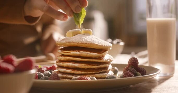 Unknown chef with refined taste aesthetically decorates elegant perfect stack of pancakes with sprig of mint herbs. Advertising cinematic. Delight in cozy morning scrumptious gluten-free breakfast
