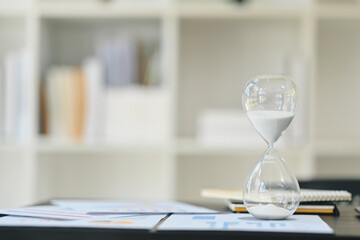 Hourglass on wooden office table with financial documents. Time management concept