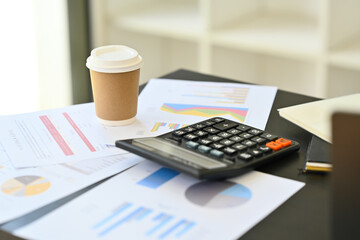 Financial analyst workplace with calculator machine, notepad, documents and paper cup on table