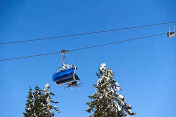 Chairlift of ropeway against blue sky. Cable car transports winter ski and snowboard riders....