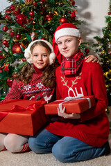 Children with gifts in their hands sit near the Christmas tree.