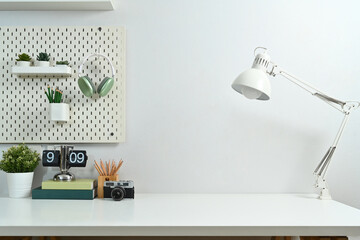 Creative workplace with lamp, camera, lamp, books, houseplant and peg board on wall