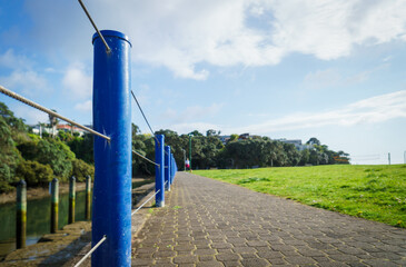 Fototapeta na wymiar Unrecognizable people walking the dog at Milford Beach Reserve. Selective focus on the blue handrail post along the wateredge. Milford. Auckland.