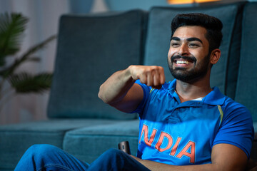 excited Young man Celebrating Indian cricket team victory while watching on tv at home - concept of Winning Happiness, Emotional moments and entertainment. - obrazy, fototapety, plakaty
