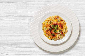 portion of macaroni and cheese with corn, bacon topped with panko breadcrumbs on white plate on white wooden table, horizontal view from above, flat lay, free space