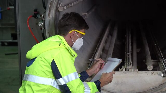 technician engineer worker wear mask holding clipboard sitting to checking boiler tank in factory