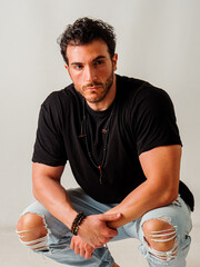 A man crouching on the ground wearing ripped jeans, in studio, on white background
