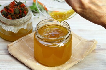 Pouring melted natural beeswax into warm herbal ointment. Woman hand holding a bowl with bee wax....