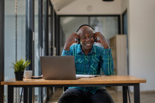 Senior Black Man Wearing Headphones Enjoying Listening To Music Or Something Interesting To Relax While Working.