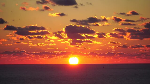 A red burning sunset over sea. Abstract nature summer ocean sea background. Small waves on golden warm water surface with bokeh lights from sun. Weather and climate change