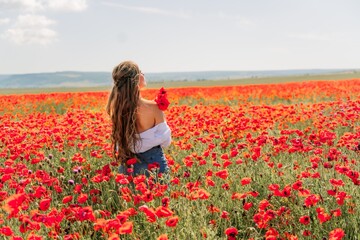 Fototapeta na wymiar Woman poppies field. Back view of a happy woman with long hair in a poppy field and enjoying the beauty of nature in a warm summer day.