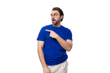 young confident brunette man with a beard dressed in a blue t-shirt shows his hand to the space for advertising on a studio white background