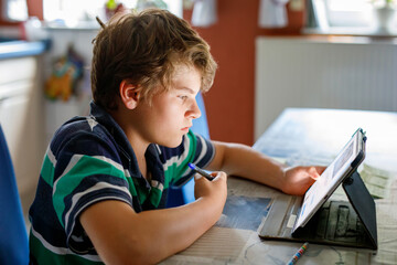 Preteen kid boy learning at home on laptop for school. School child making homework and using notebook and modern gadgets. Home schooling concept. - obrazy, fototapety, plakaty