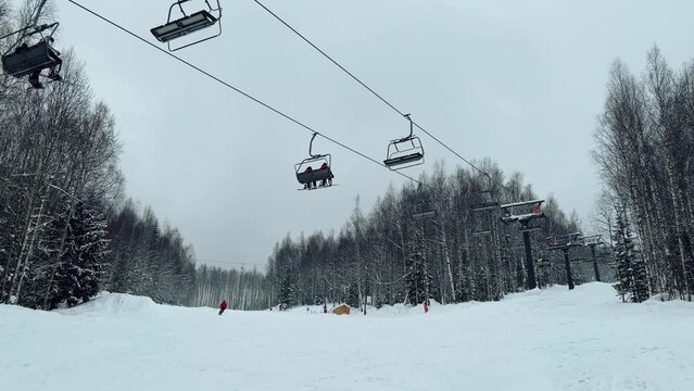 A chairlift at a ski resort on a cloudy winter day in the Ural Mountains. A lift on the background of factory pipes. Climbing the mountain. Gubakha, Perm Krai, 4K