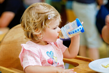 Adorable toddler girl drinking formula milk or water from bottle. Cute happy baby child taking food...