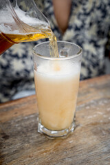 Pouring fresh beer in the glass full of froth from the jar on a wooden table.