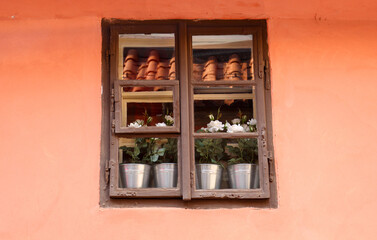 Fototapeta na wymiar Brown wooden window on a red facade, on the windowsill are flowers