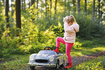 Little preschool girl driving big vintage toy car. Happy child having fun with playing outdoors....