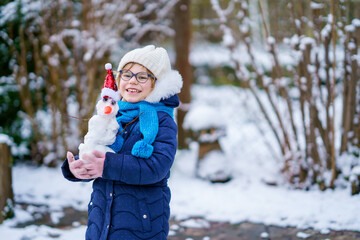 Cute little preschool girl with glasses making mini snowman. Adorable healthy happy child playing and having fun with snow, outdoors on cold day. Active leisure with children in winter