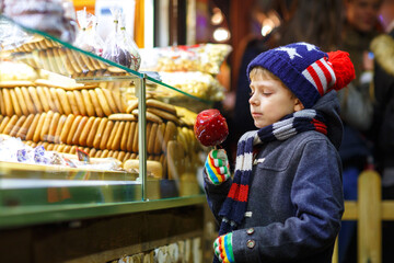 Happy child eating on apple covered with red sugar on Christmas market