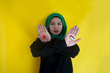 Muslim woman shows crossed arms painted with Palestinian flag and watermelon slices over yellow...