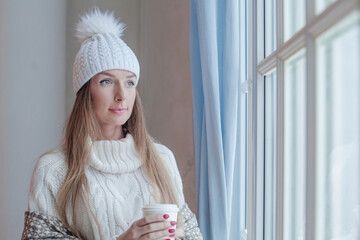Cheerful winter woman holding hot dring and resting at home, romantic portrait