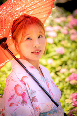 Portrait of a young woman wearing yukata summer kimono and holding Japanese umbrella in a hydrangea...