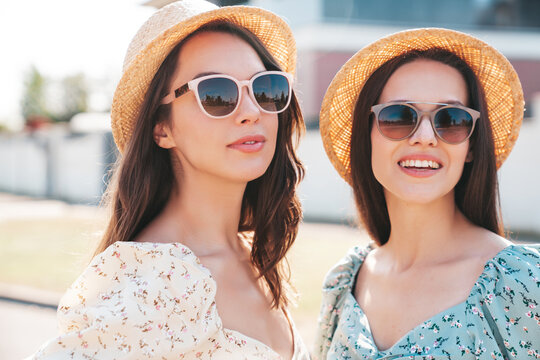 Two young beautiful smiling hipster female in trendy summer dresses  clothes. Sexy carefree women posing in the street. Positive models having fun at sunny day. Going crazy. In sunglasses