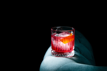 red cocktail in a transparent glass with round ice, whipped cream and black berry on top, side view