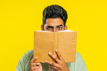 Sneaky cunning relaxed Indian young man reading interesting fairytale story book, leisure hobby, knowledge wisdom, education, learning, study, wow. Arabian Hindu guy isolated on yellow background - obrazy, fototapety, plakaty