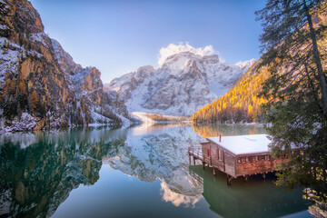 Le lago di Braies (lac de Braies) dans les Dolomites en Italie en hiver avec le reflet de la montagne dans le lac et le célèbre chalet et son ponton qui permettent l'acces aux barques de loisirs. - obrazy, fototapety, plakaty