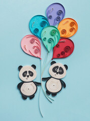 Funny pandas quilling characters on blue background. Happy cute panda flying with colorful balloons. Party elements. Happiness, dreaming and freedom concept. Hand made of paper quilling technique.