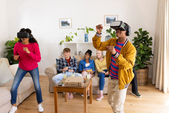 Happy diverse group of teenage friends with pizza using vr headsets and playing at home