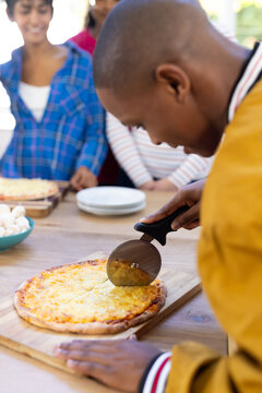Happy diverse group of teenage friends cooking and cutting pizza in kitchen