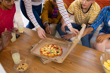 Happy diverse group of teenage friends sitting on couch and eating pizza