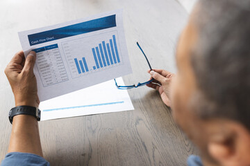 Senior biracial man holding glasses and checking documents at home