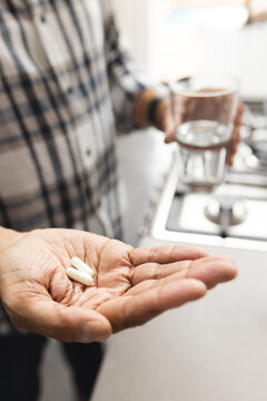Senior biracial man holding glass of water and taking pills at home