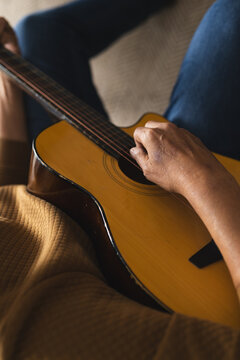Senior biracial man sitting on couch and playing guitar at home