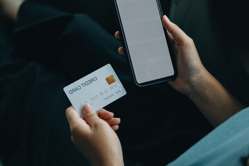 A credit card in the hands of a young businesswoman pays for a business on a mobile phone and on a desk with a laptop.