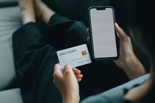 A credit card in the hands of a young businesswoman pays for a business on a mobile phone and on a desk with a laptop.