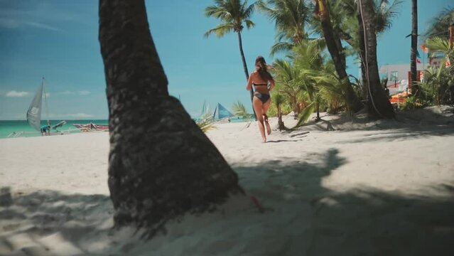 Woman running white sand beach, palm trees, tropical Borakay island, Philippines. Long hair slim caucasian brunette relax, enjoy outdoor sport lifestyle, travel on summer holiday vacation. Slow motion