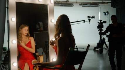 The actress is preparing to film a movie. She sits in front of a mirror on the set and applies makeup to herself. Backstage concept - obrazy, fototapety, plakaty