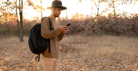 A traveler in a hat catches a connection and the Internet while standing in the forest at sunset....