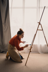 Beautiful female painter in art studio. Young talented artist working in workshop over window...
