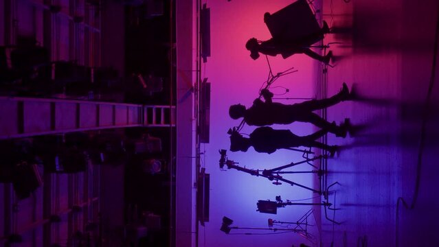 Professional filming pavilion with a neon cyclorama. The process of preparing for the shooting of a music video. Director, Cameraman and crew in Backstage. Vertical video