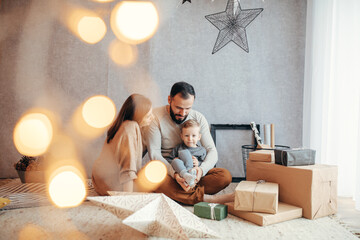 A Young Family Unwrapping Christmas Gifts in a Festively Adorned Home with Glowing Lights and a...