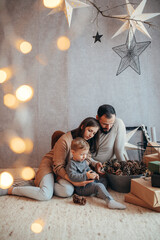 Young Family, Their 2-Year-Old Blond Boy, Amidst Christmas Gifts and Lights in Their Home Decorated...