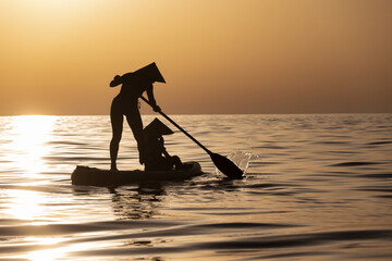 a woman with a child on a sup board in the sea swim against the background of a beautiful sunset,...