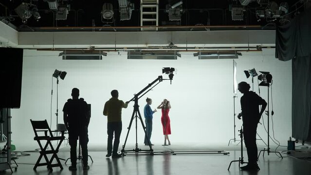 Professional filming pavilion with a white cyclorama. The process of preparing for the shooting of a music video. Director, Cameraman and crew in Backstage.